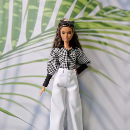 Close-up of a brunette doll modeling fashionable clothes for Barbie, including a gingham puff-sleeve blouse and high-waisted white pants.