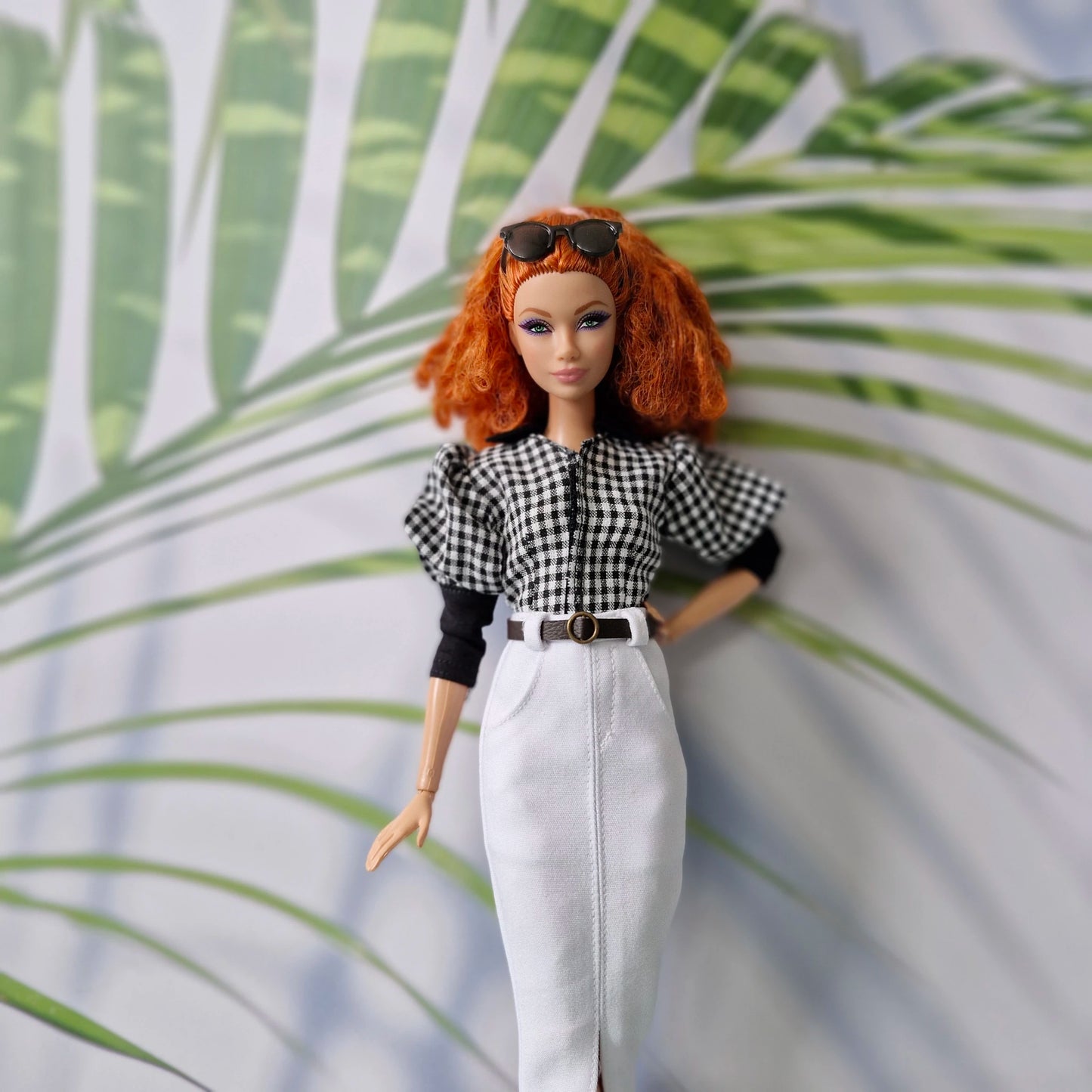 Close-up of stylish clothes for Barbie, showing a gingham puff-sleeve shirt and elegant white midi skirt.