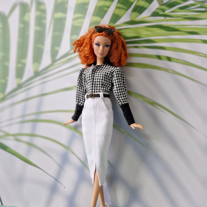 Redhead doll posing in office clothes for Barbie, featuring a checkered top, sunglasses, and long white skirt.