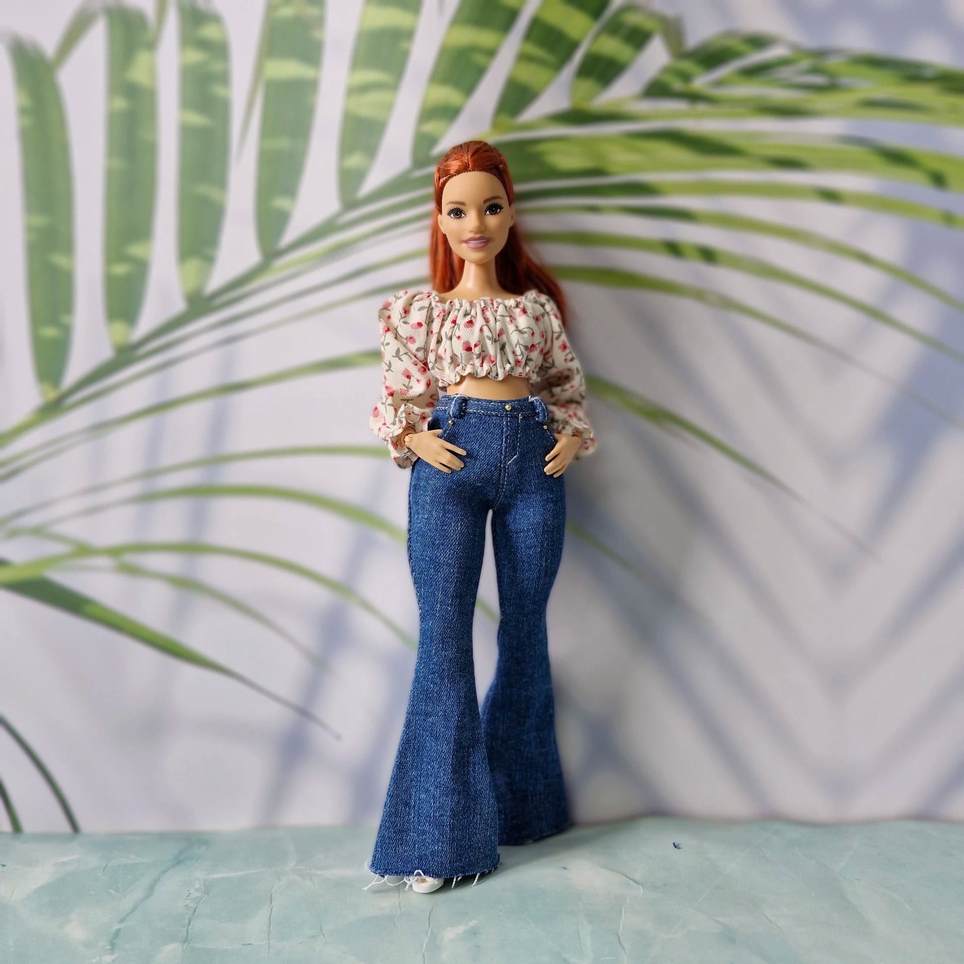Redhead doll with hands in pockets wearing a pink floral blouse and dark wash flared jeans for Curvy Barbie.