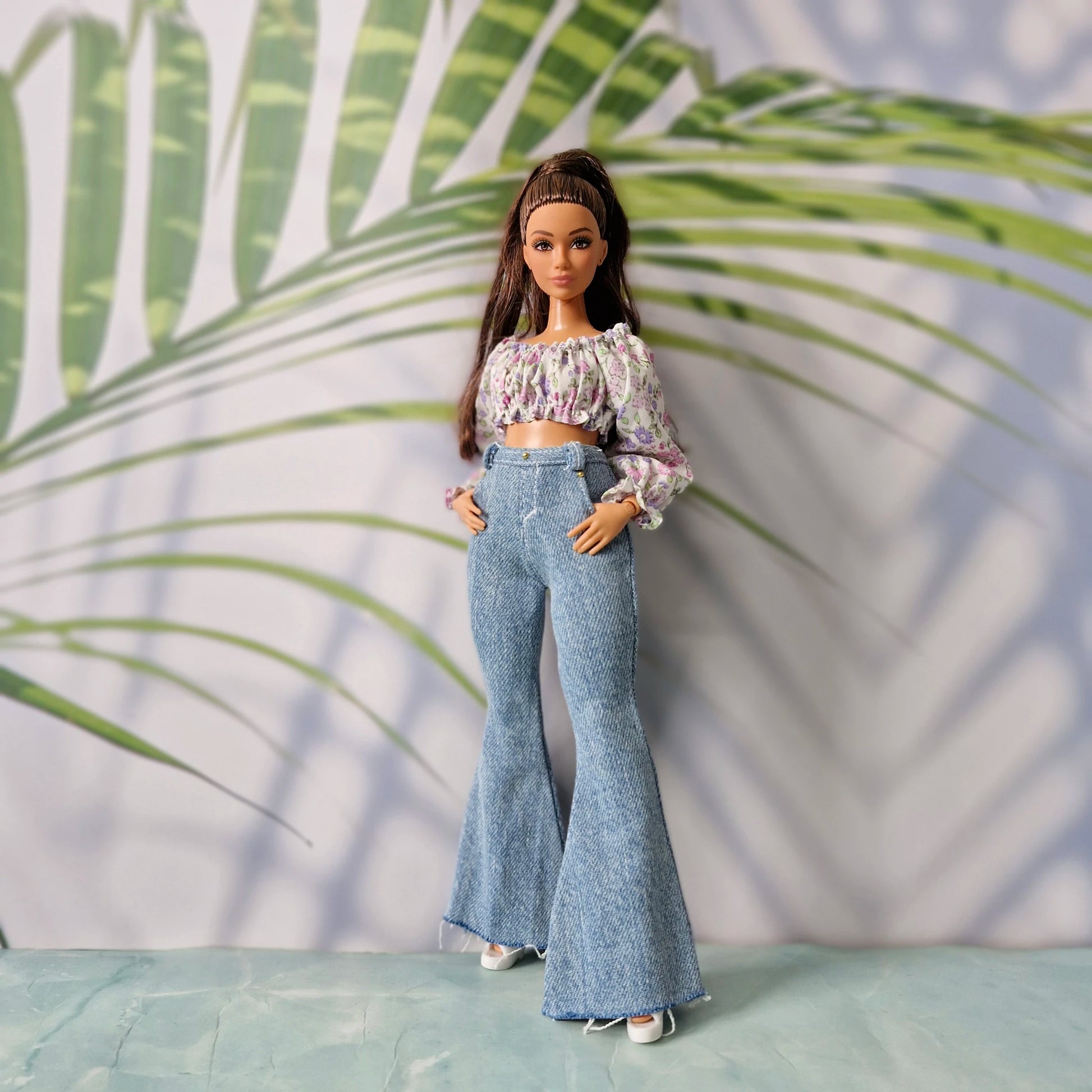 Full body shot of a doll in stylish casual clothes for Curvy Barbie, including a purple floral top and light wash jeans.