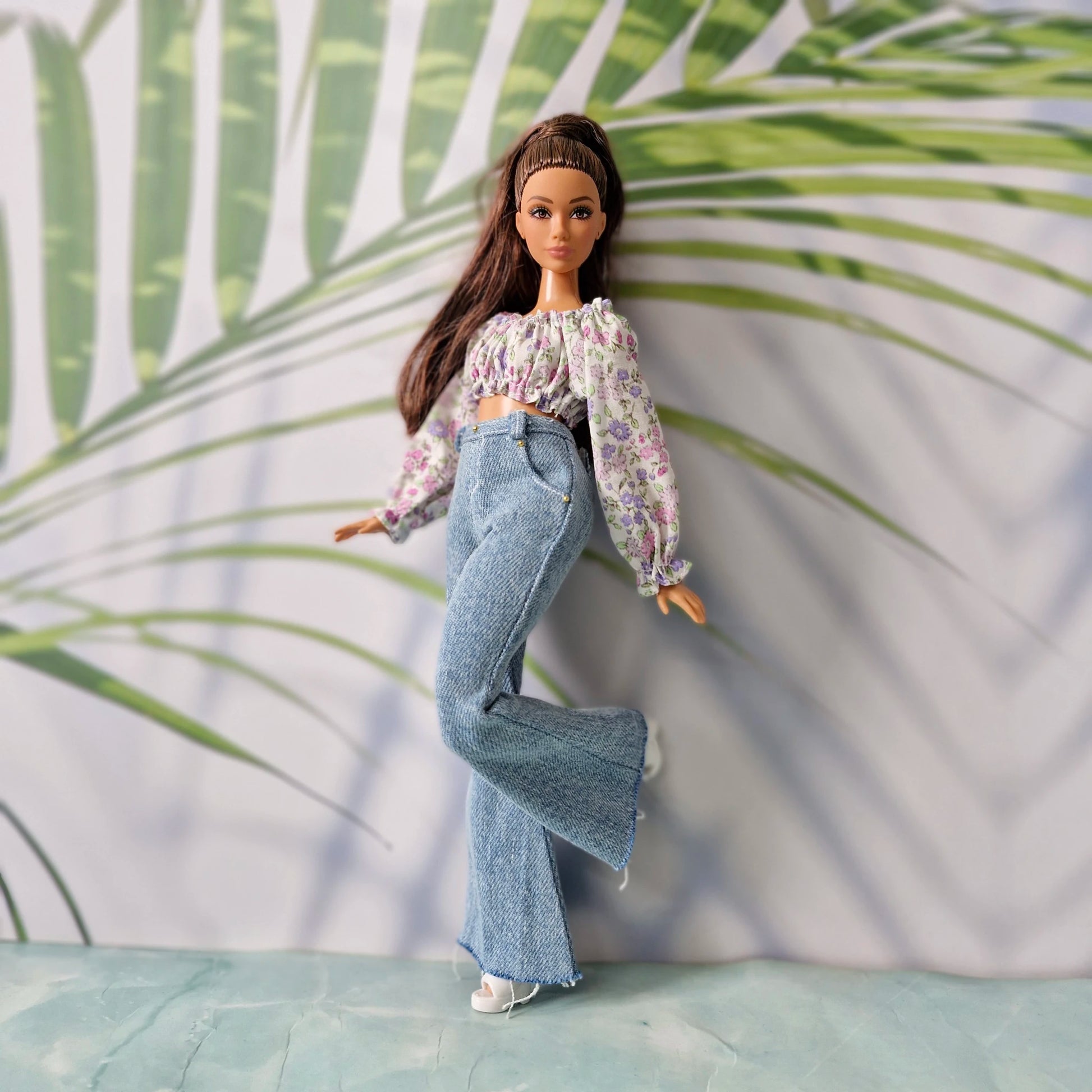 Fashionable clothes for Curvy Barbie showcased by a brunette doll in a purple floral shirt and light blue flared pants.