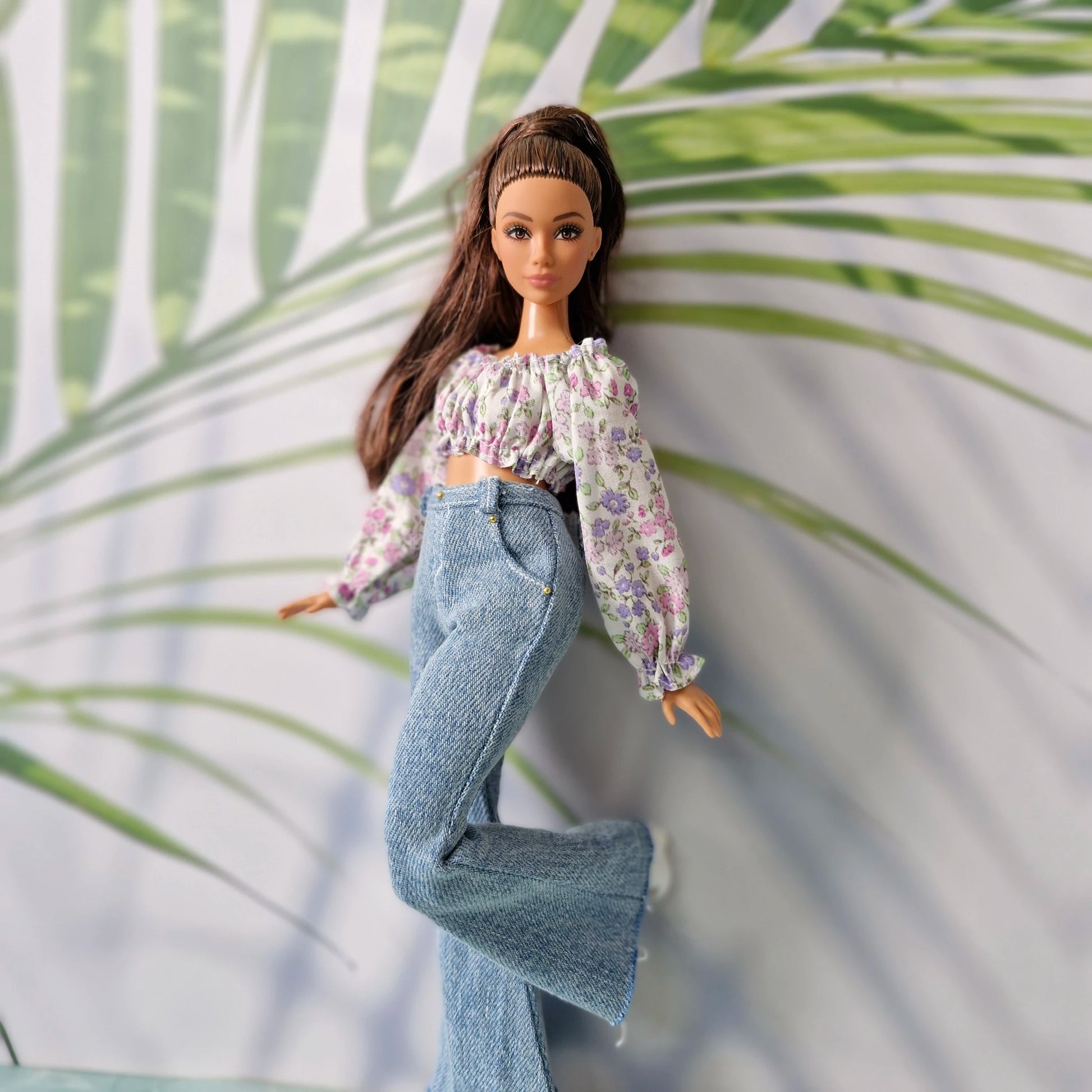 Doll posing playfully in a chic outfit for Curvy Barbie, featuring a floral crop top and stylish light denim jeans.