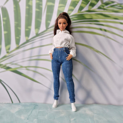 Brunette fashion doll with hands in pockets wearing a white hoodie and dark wash skinny jeans for Curvy Barbie.