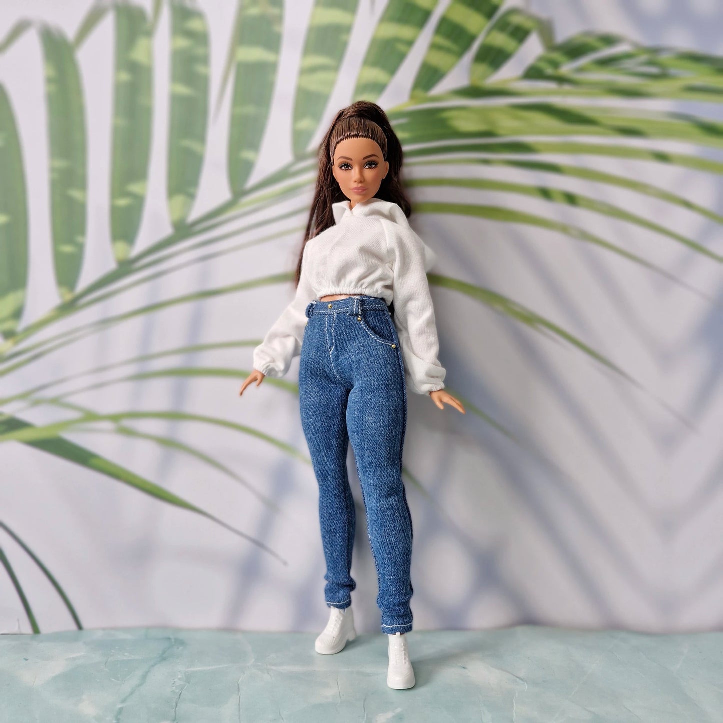 Close-up of a doll modeling a white long-sleeve crop hoodie and high-waisted dark denim jeans for Curvy Barbie.