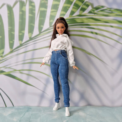 Close-up of a doll modeling a white long-sleeve crop hoodie and high-waisted dark denim jeans for Curvy Barbie.