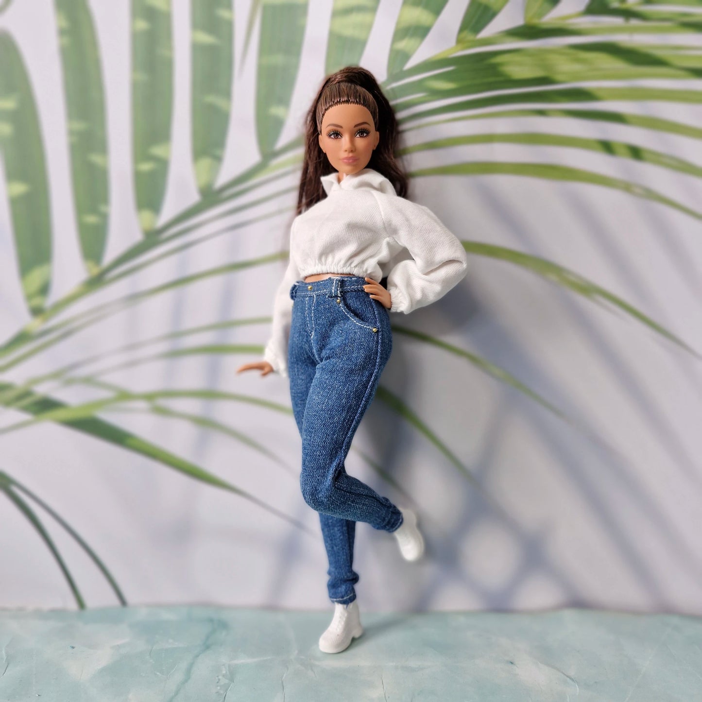 Brunette doll wearing a white crop hoodie and dark blue skinny jeans for Curvy Barbie, posing casually.