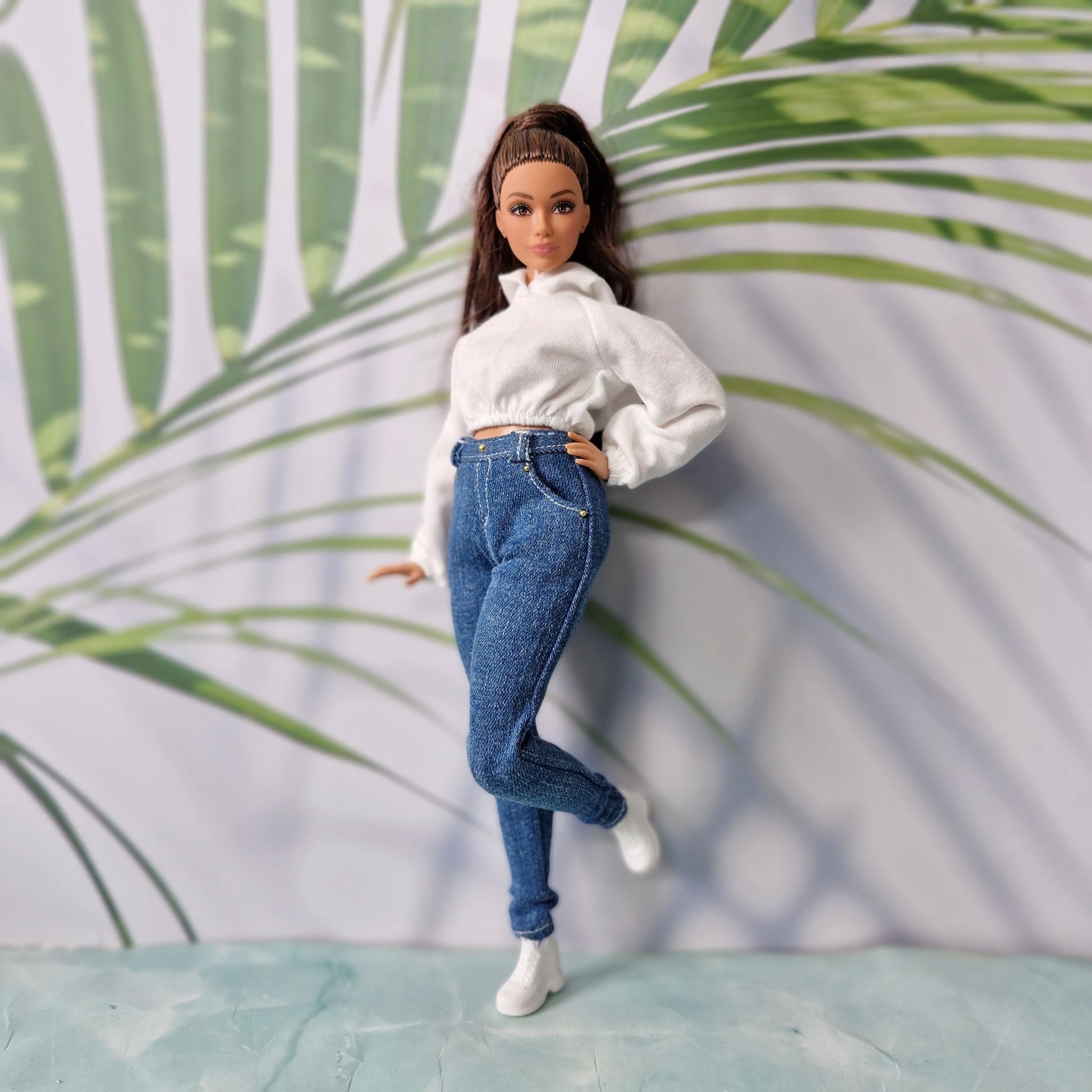 Brunette doll wearing a white crop hoodie and dark blue skinny jeans for Curvy Barbie, posing casually.