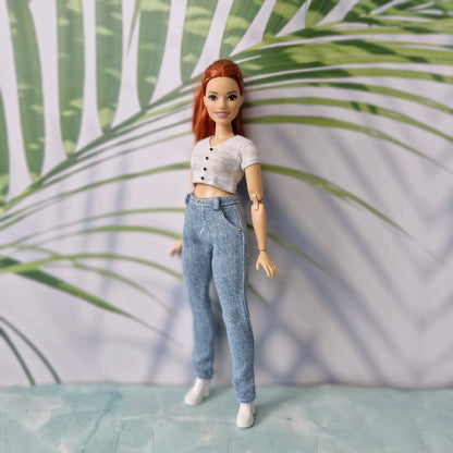 Curvy fashion doll standing straight, modeling a trendy grey short-sleeve shirt and light blue pants for Curvy Barbie.