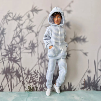 A doll or mannequin wearing a light blue and white striped hooded sweatshirt and matching pants, standing against a gray wall with bamboo silhouettes.