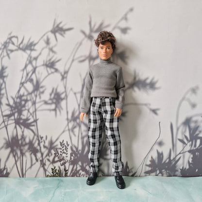 Full body view of a doll wearing a grey turtleneck and black and white plaid pants for Ken.