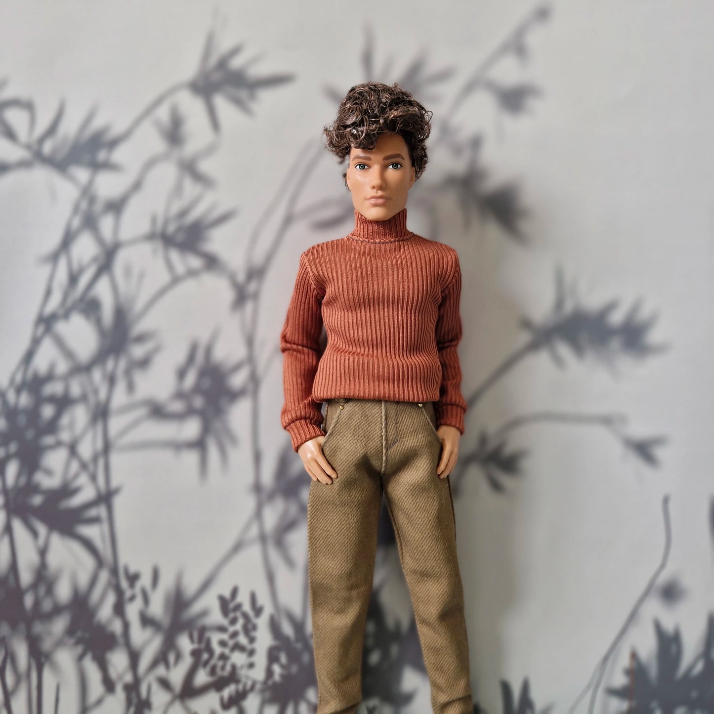 Ken doll wearing a burnt orange long-sleeve turtleneck sweater and plain tan trousers for Ken.