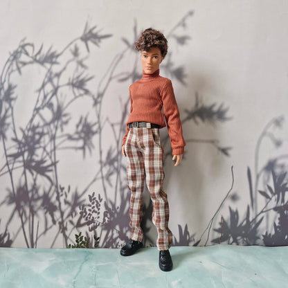 Full body shot of a male fashion doll wearing a brown sweater and plaid trousers for Ken.