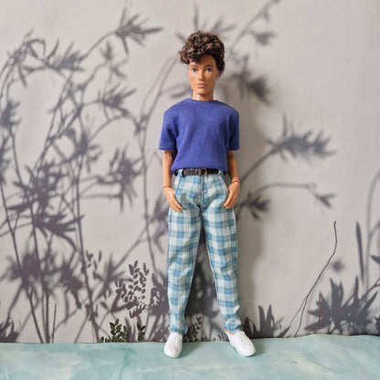 Ken doll standing in a casual blue short-sleeve t-shirt and light blue plaid pants for Ken.