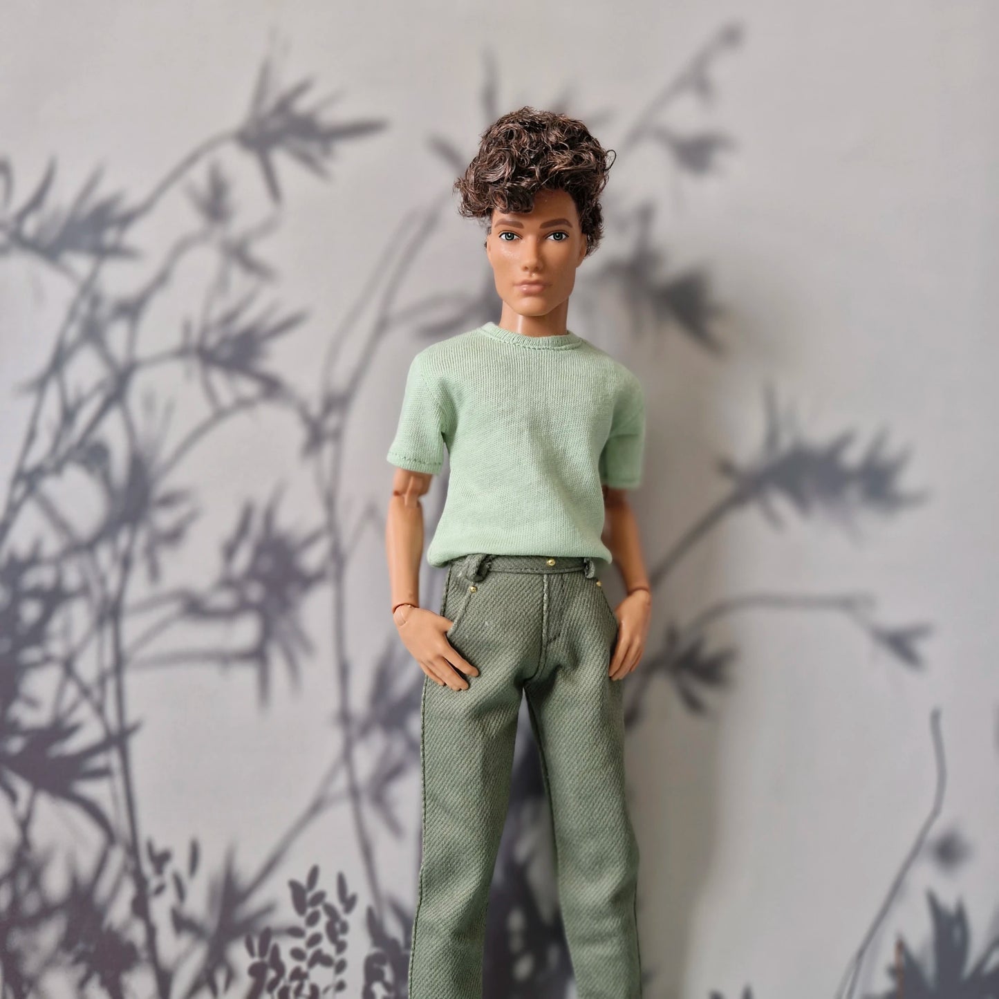 Ken doll modeling a mint green short-sleeve t-shirt and solid olive green pants for Ken.