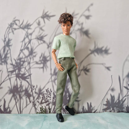Full body shot of a doll wearing a mint green t-shirt, plain olive pants, and black shoes for Ken.