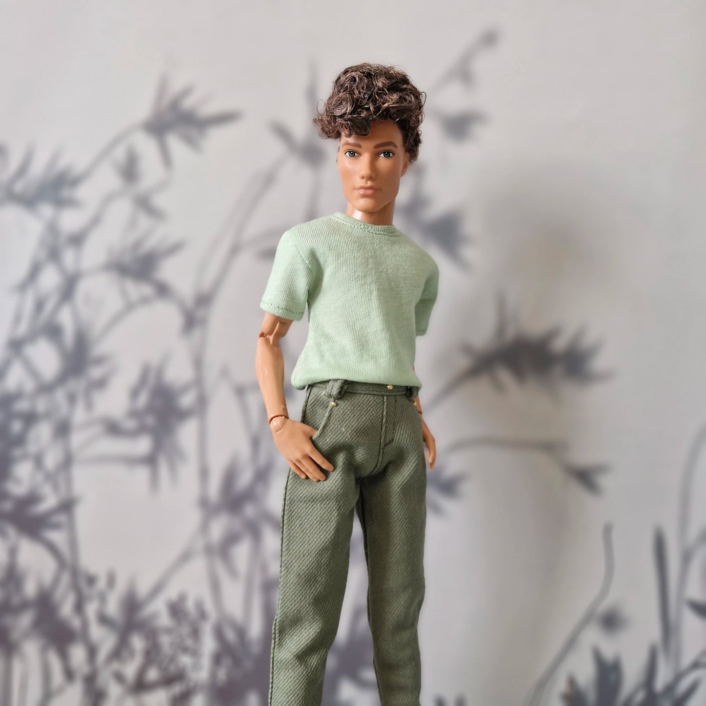 Close up of a mint green short-sleeve top and solid olive green pants for Ken.