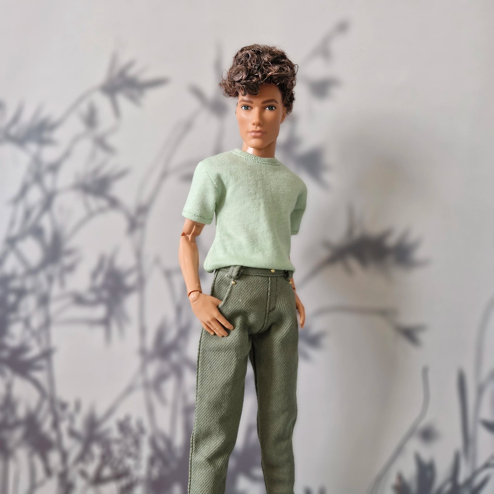 Close up of a mint green short-sleeve top and solid olive green pants for Ken.