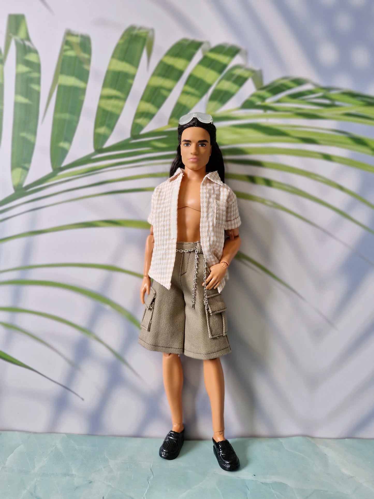 Long-haired 1/6 scale male doll wearing an unbuttoned beige gingham shirt and khaki cargo shorts with a chain for Ken.