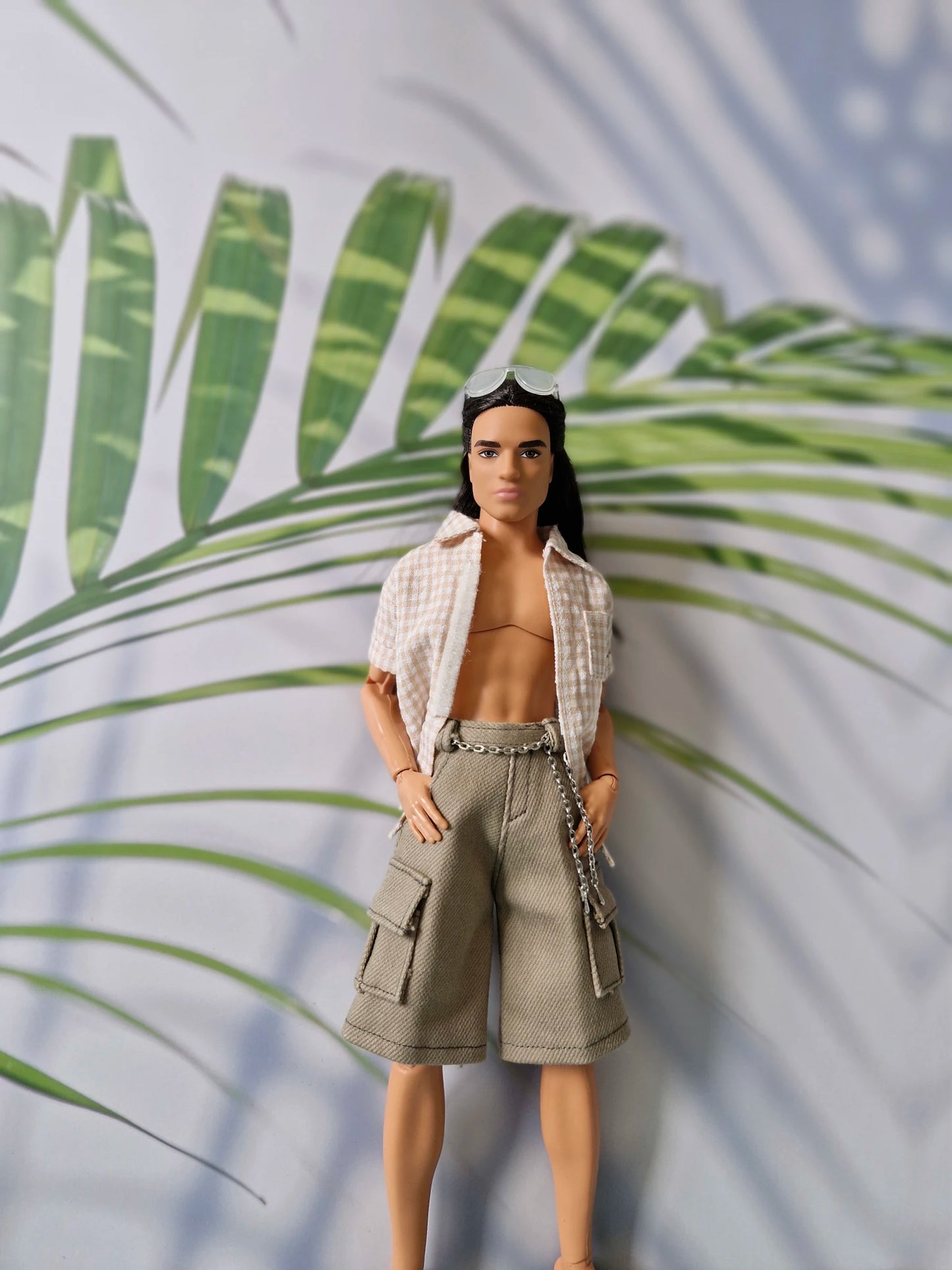 Male doll posing in a casual unbuttoned beige top and khaki cargo shorts with chain details for Ken.