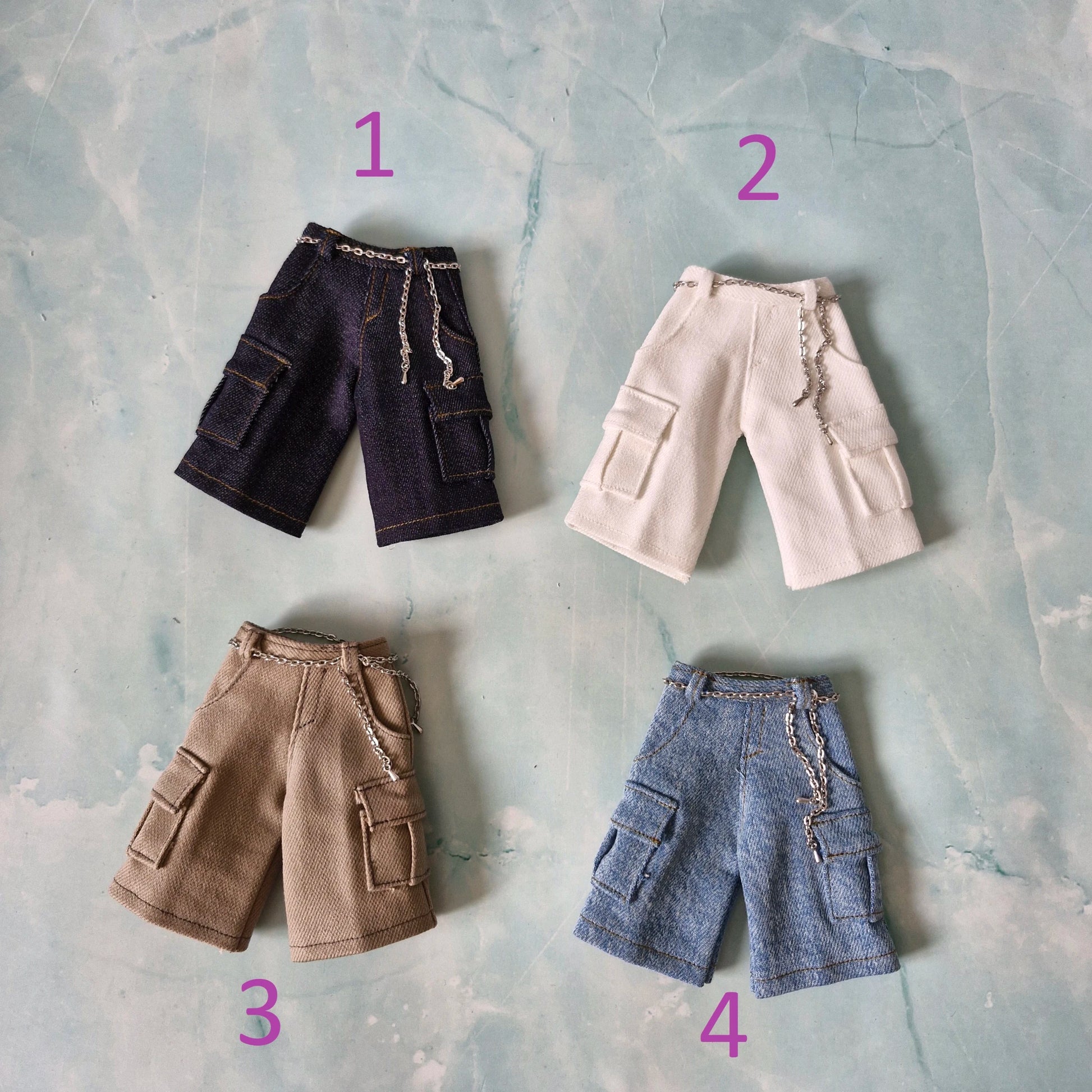 Flat lay of four 1/6 scale doll cargo shorts with chains in dark denim, white, khaki, and light denim for Ken.
