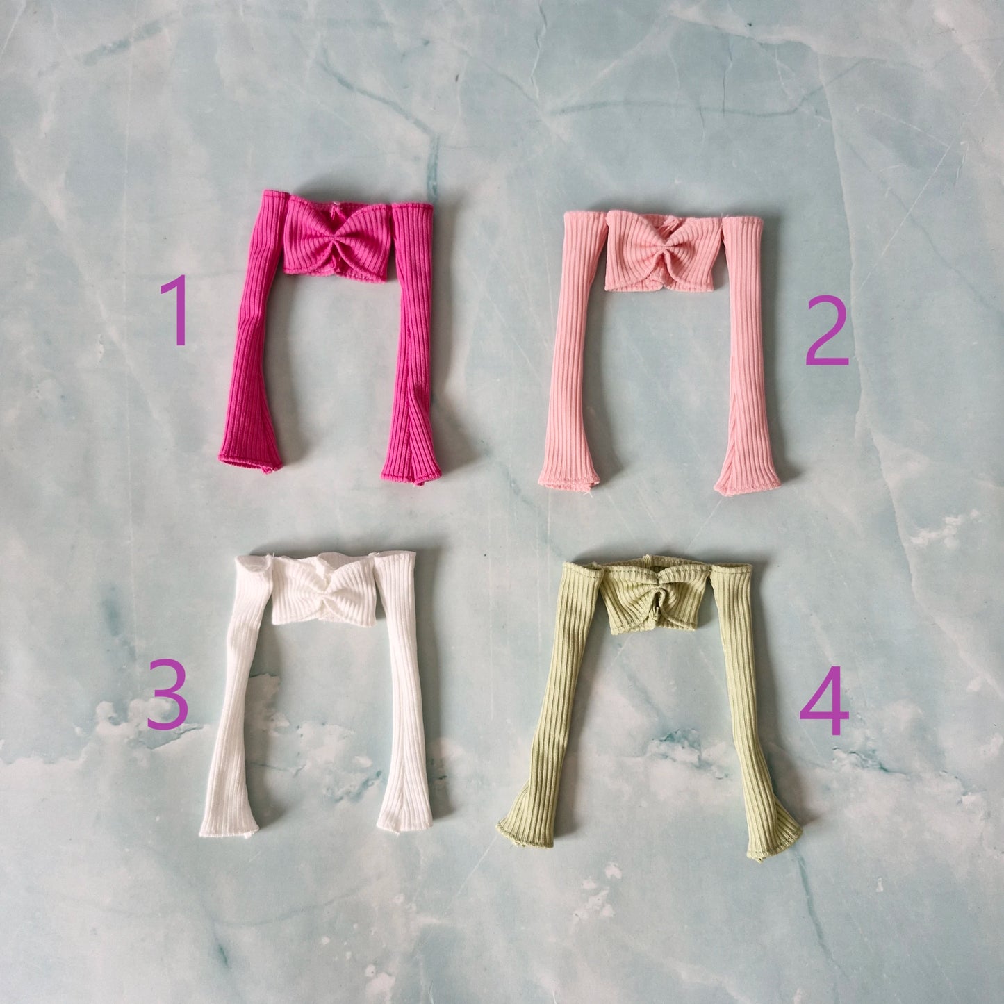 Flat lay of four 1/6 scale off-shoulder long-sleeve tops in dark pink, light pink, white, and green for Barbie.