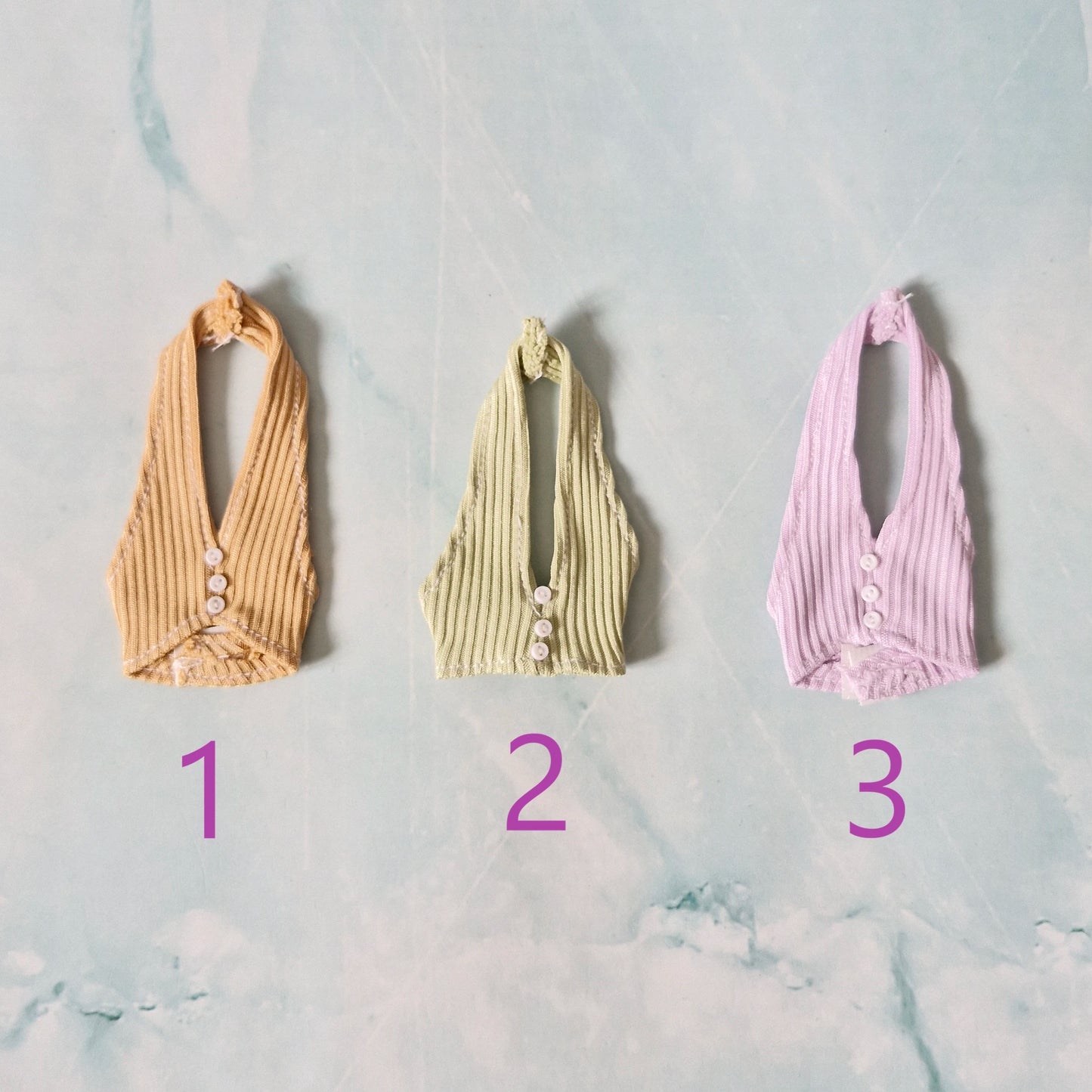 Flat lay of three 1/6 scale doll ribbed halter tops in yellow, green, and lilac sold separately for Barbie.
