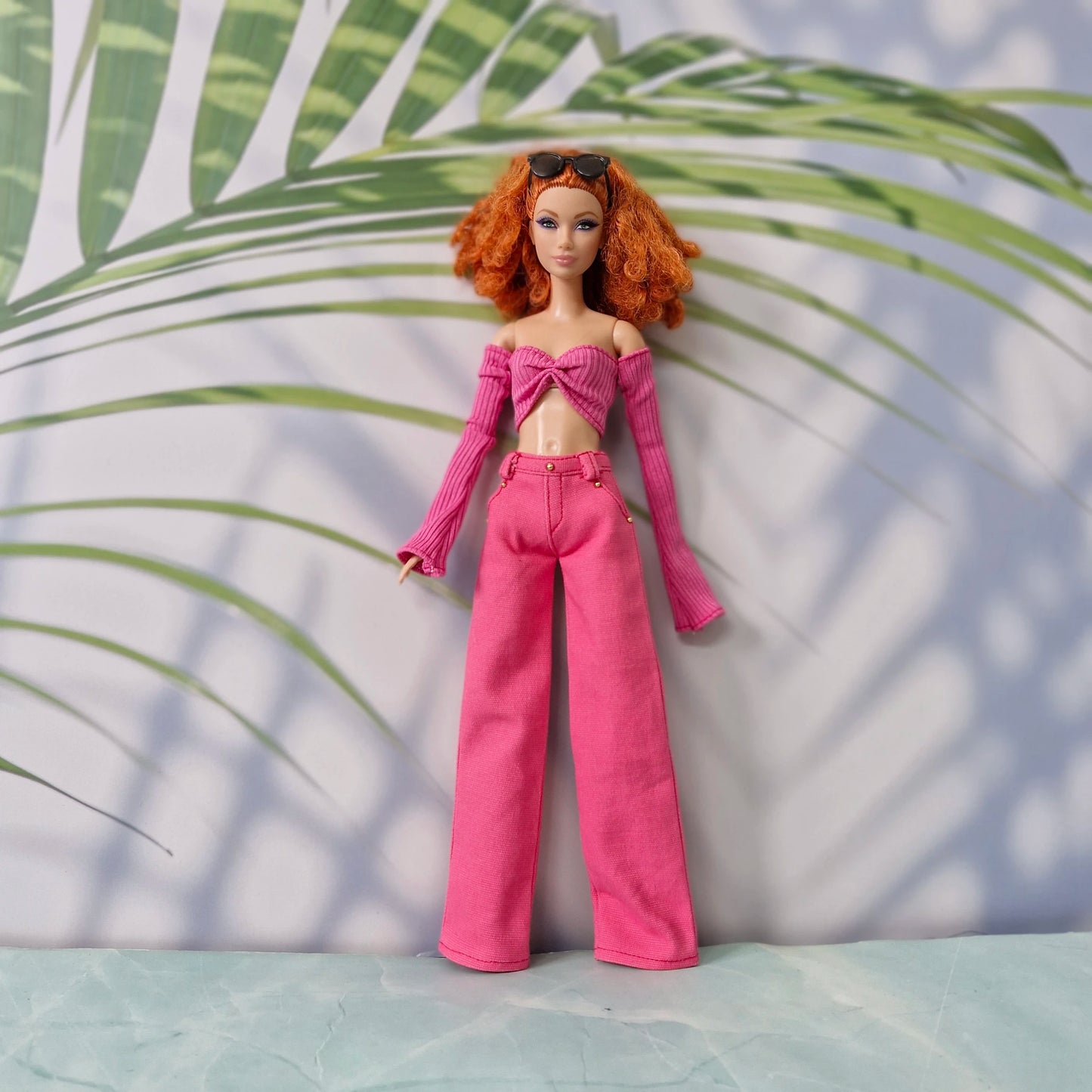 Red-haired Barbie doll wearing a dark pink off-shoulder long-sleeve top and pink wide-leg pants.