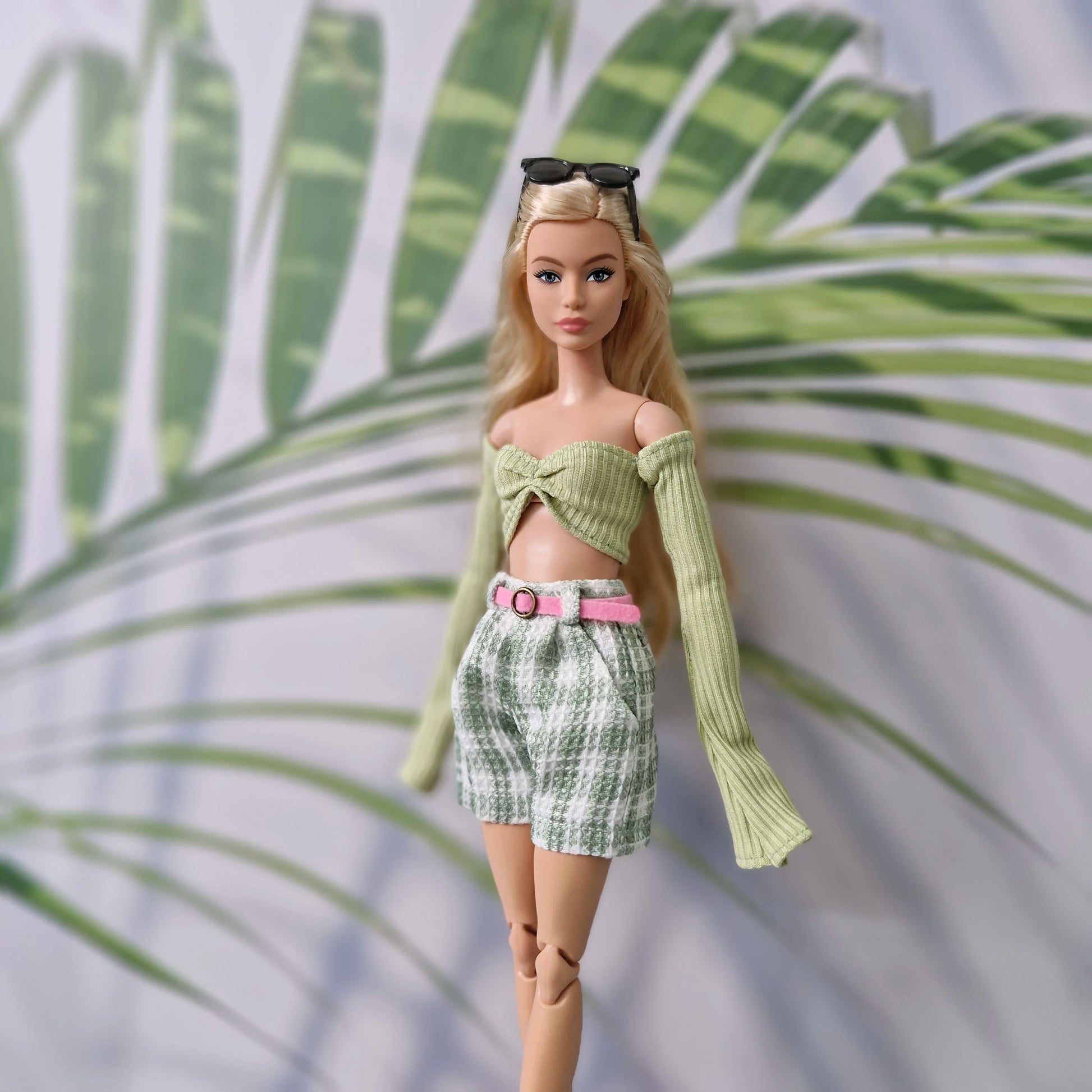 Blonde Barbie doll wearing a green long-sleeve off-shoulder top and green plaid shorts with a pink belt.