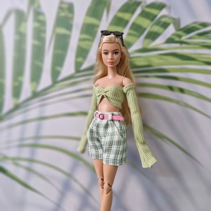 Blonde Barbie doll wearing a green long-sleeve off-shoulder top and green plaid shorts with a pink belt.