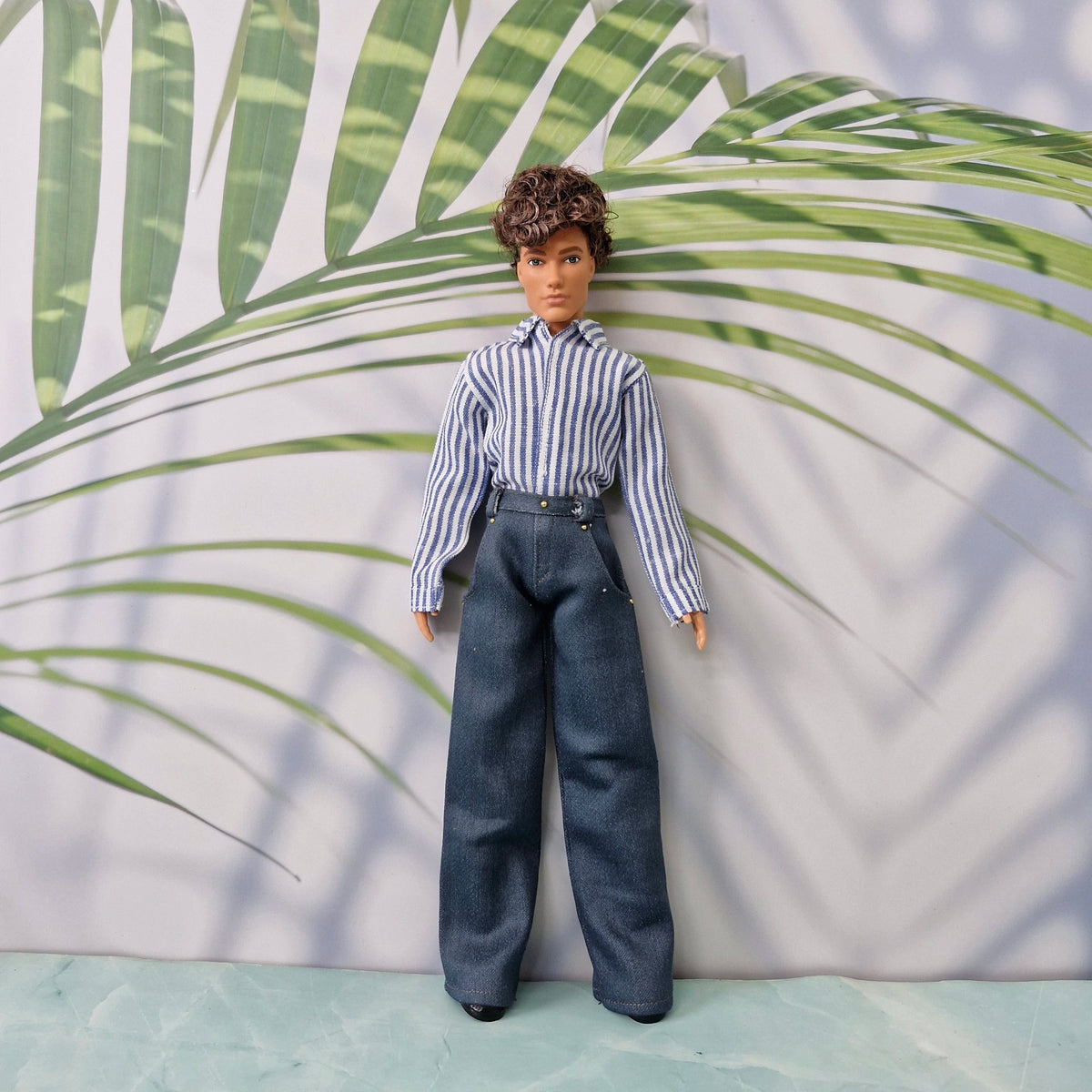 Full body shot of a Ken doll in a handmade blue vertical striped shirt and dark blue trousers.