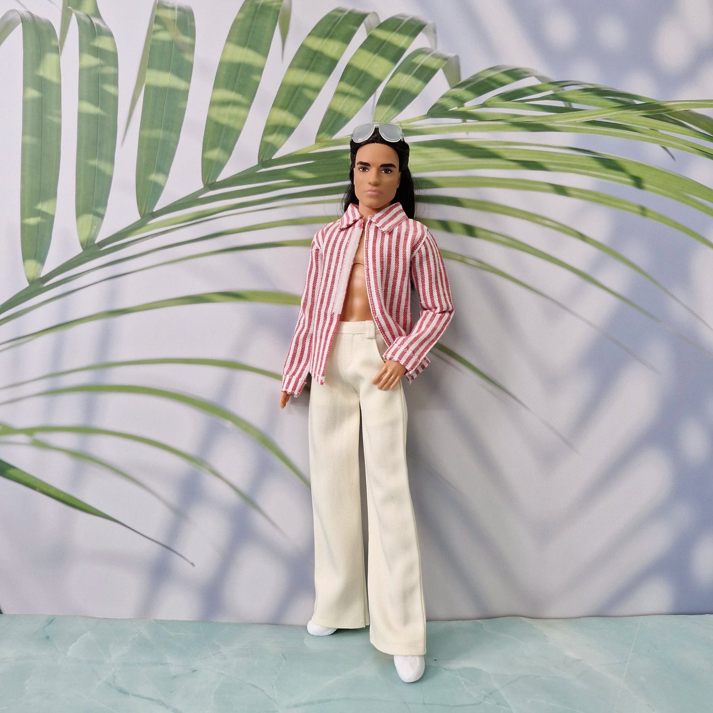 1/6 scale Ken doll wearing an unbuttoned red striped shirt and cream tailored pants.
