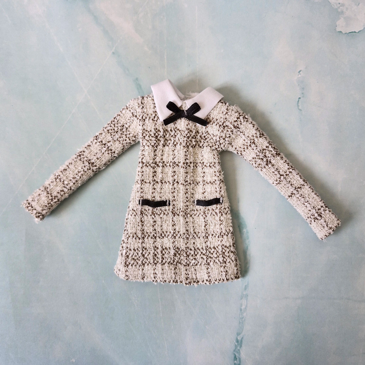 Flat lay of a handmade 1/6 scale black and white tweed dress with a white collar and black bow for Barbie.
