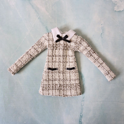 Flat lay of a handmade 1/6 scale black and white tweed dress with a white collar and black bow for Barbie.
