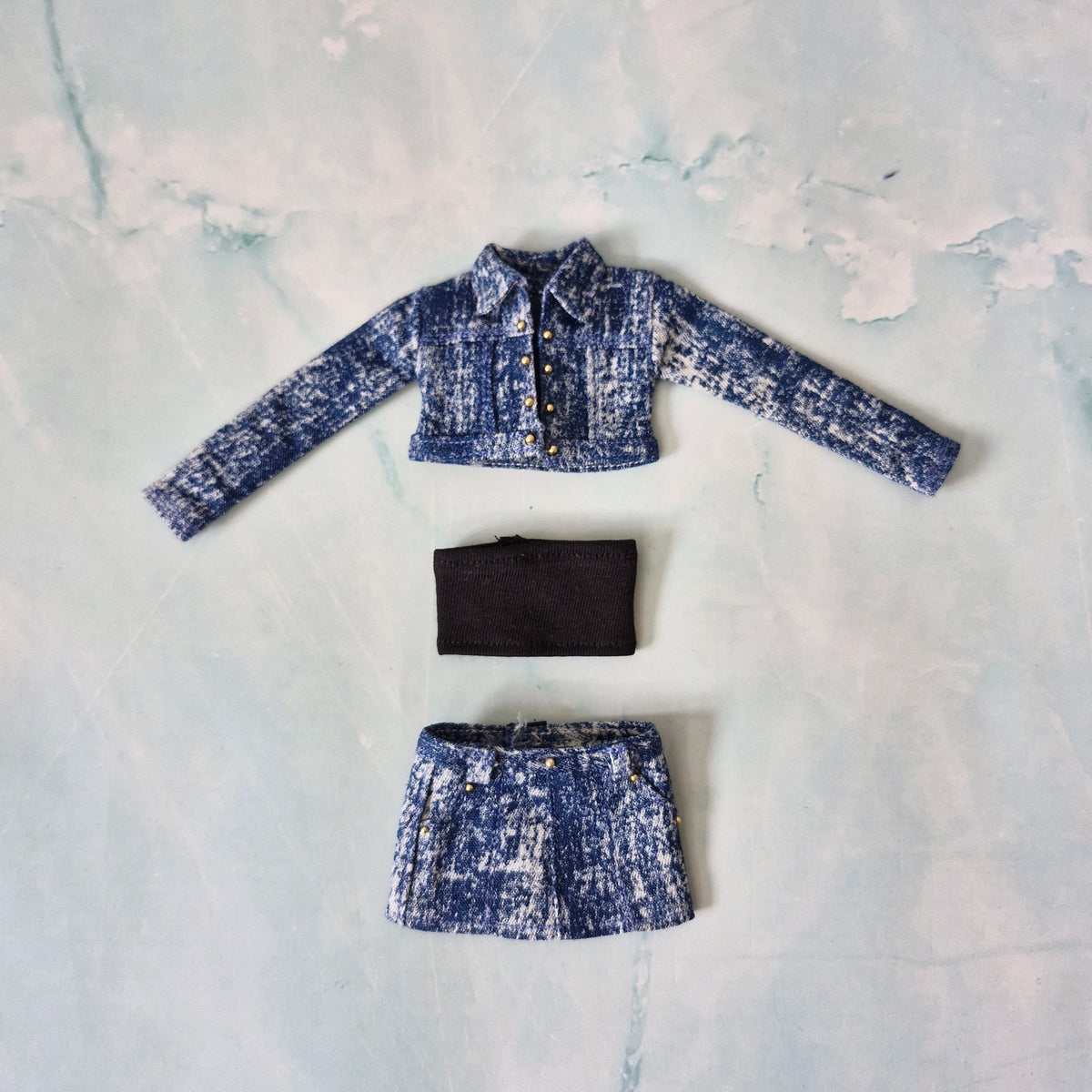 Flat lay of a handmade 1/6 scale medium acid wash denim jacket, black tube top, and matching denim skirt for Curvy Barbie.