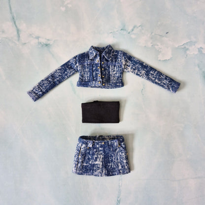 Flat lay of a handmade 1/6 scale medium acid wash denim jacket, black tube top, and matching denim skirt for Curvy Barbie.