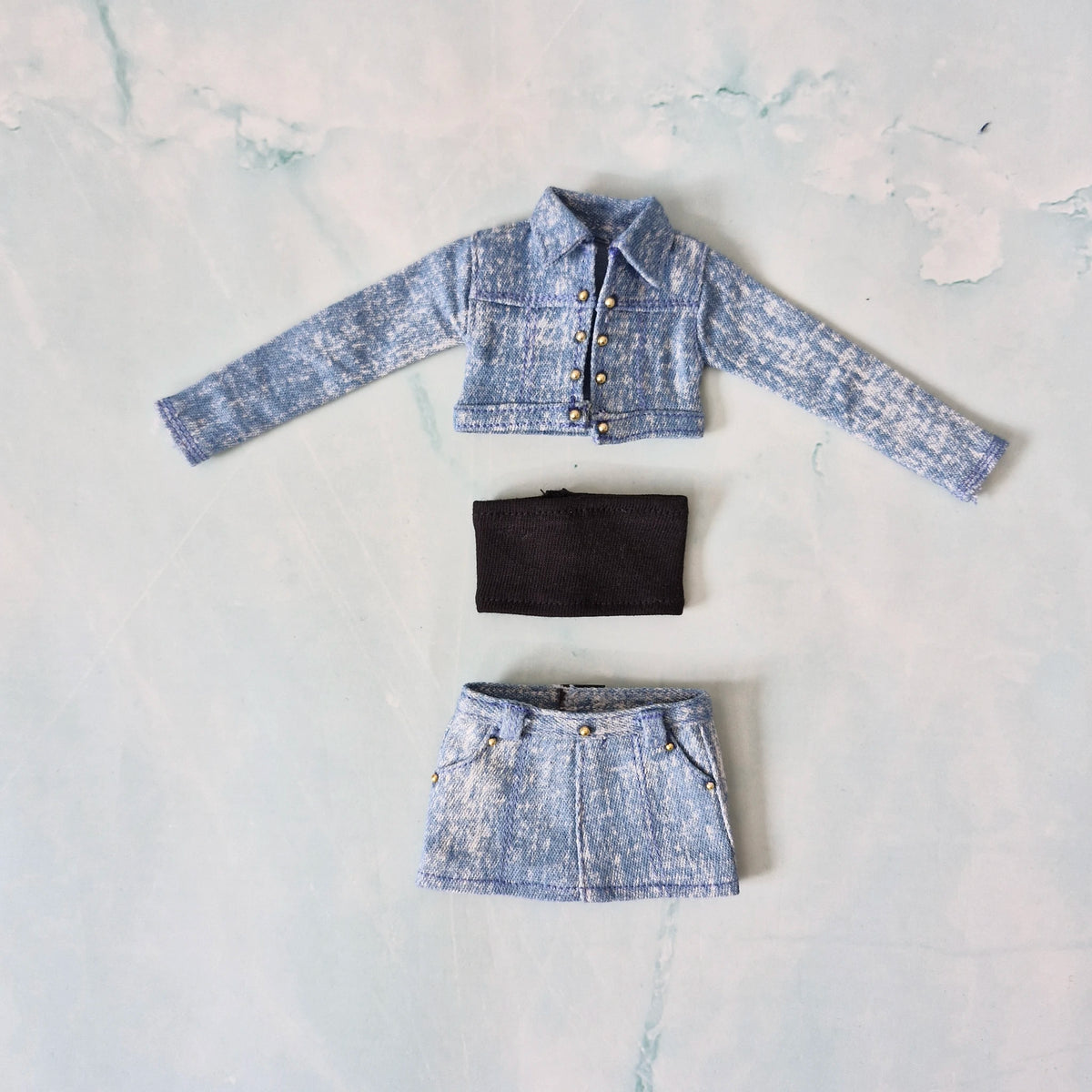 Flat lay of a 3-piece Curvy doll outfit featuring a light blue denim jacket, black tube top, and light blue denim skirt.