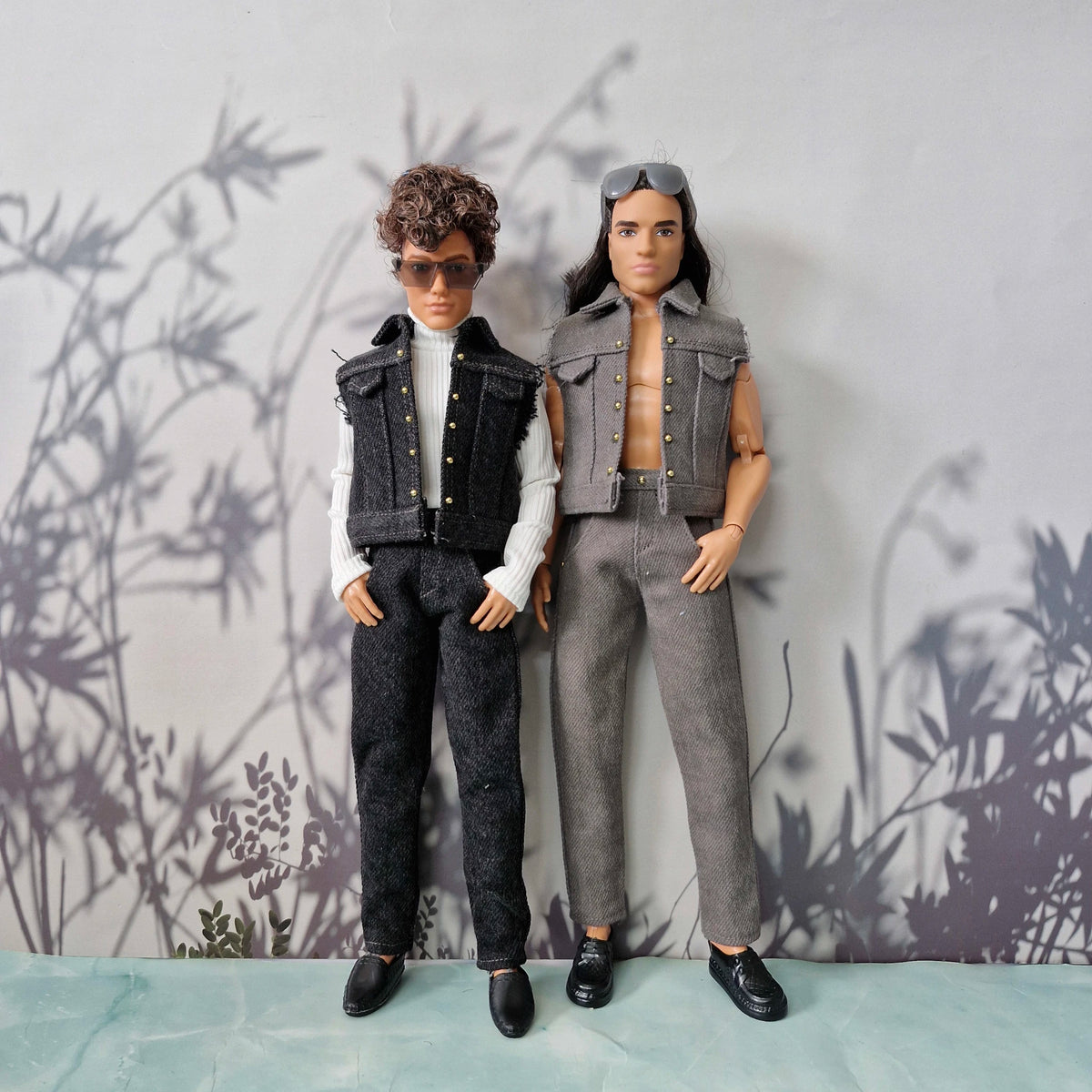 Two Ken dolls standing together; one wearing a white turtleneck and dark denim outfit, the other in a grey denim vest and jeans.