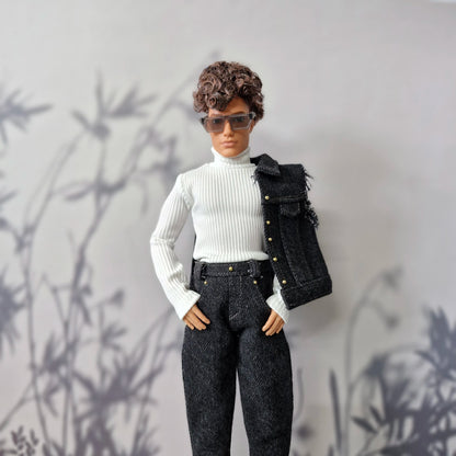 Ken doll modeling a white turtleneck top, dark wash jeans, and a dark denim vest slung over his shoulder.