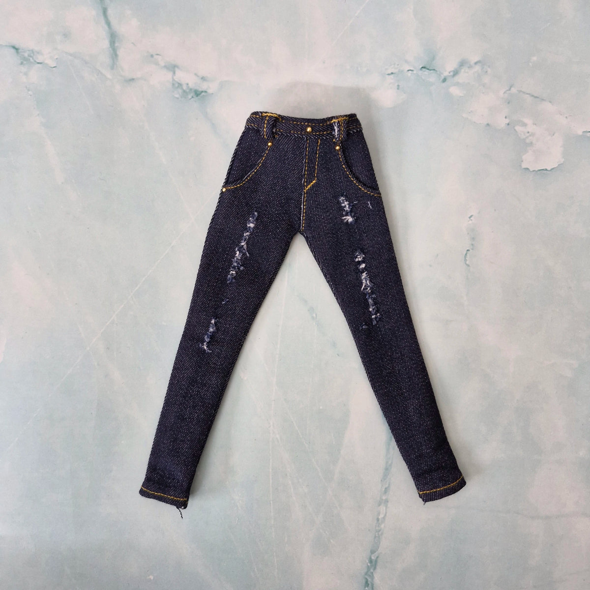 Flat lay of handmade 1/6 scale dark blue distressed denim jeans for Curvy Barbie.