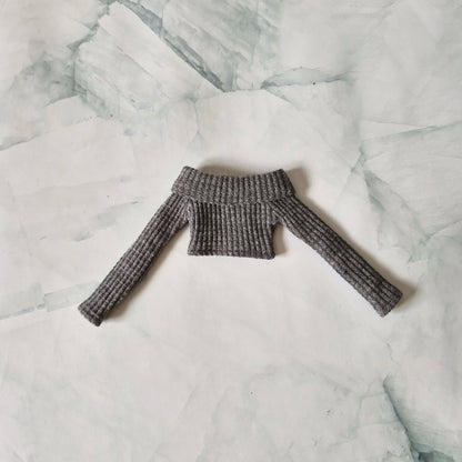 Flat lay of grey ribbed knit off-shoulder long-sleeve crop top sweater for fashion dolls on a marble background.
