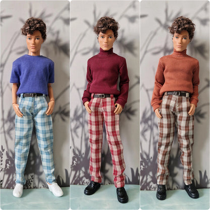 Three dolls with short curly brown hair are shown side by side wearing different color options of a ribbed turtleneck sweater and plaid pants. The left doll wears a blue sweater and light blue plaid pants, the middle doll wears a burgundy sweater and red plaid pants, and the right doll wears a rust orange sweater and brown plaid pants.