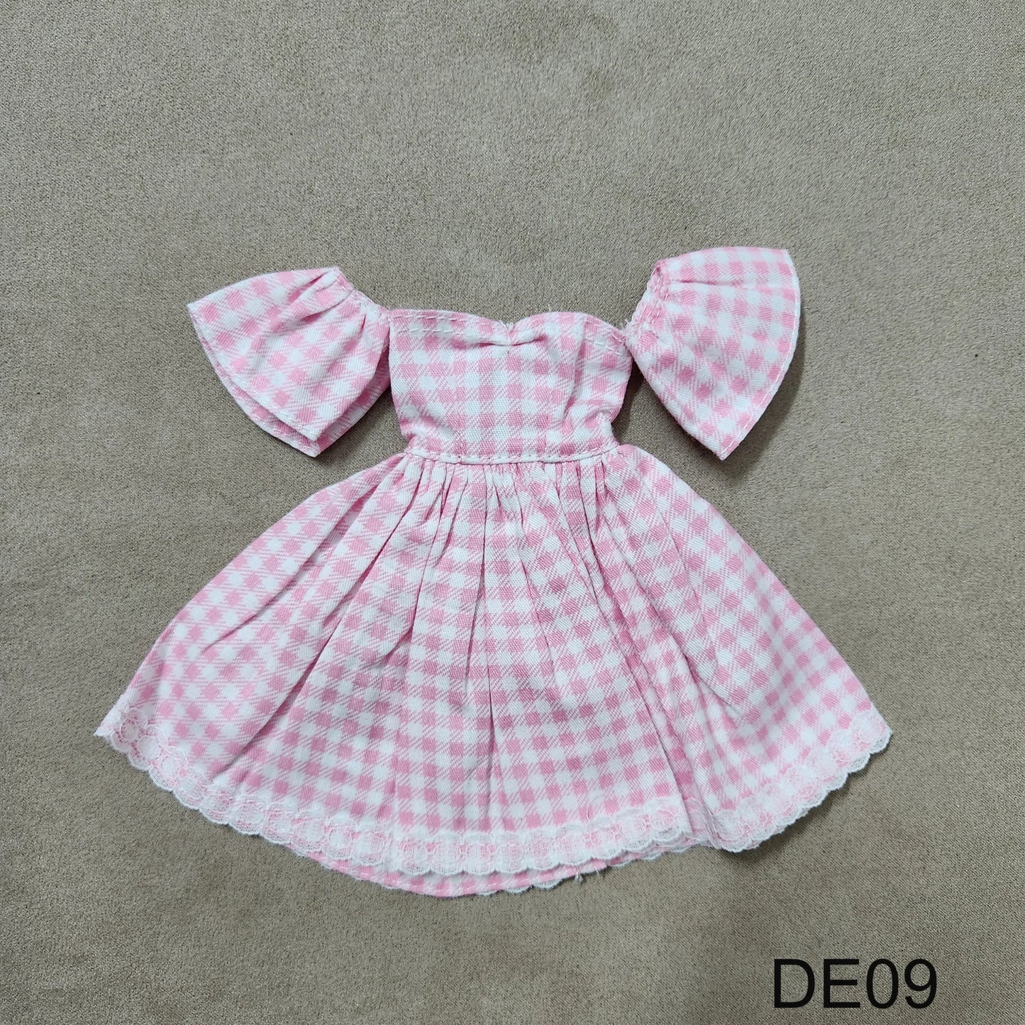 Pink gingham off-shoulder Barbie dress DE09 laid flat on fabric background