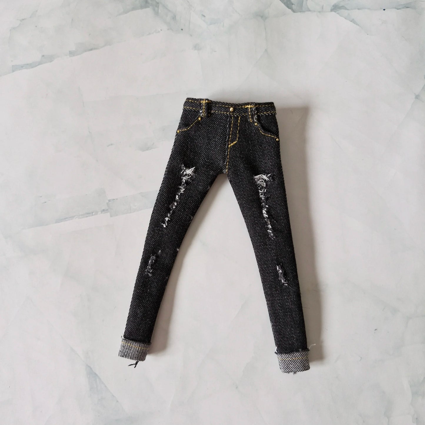 Flat lay view of black distressed skinny jeans with yellow stitching for Barbie dolls