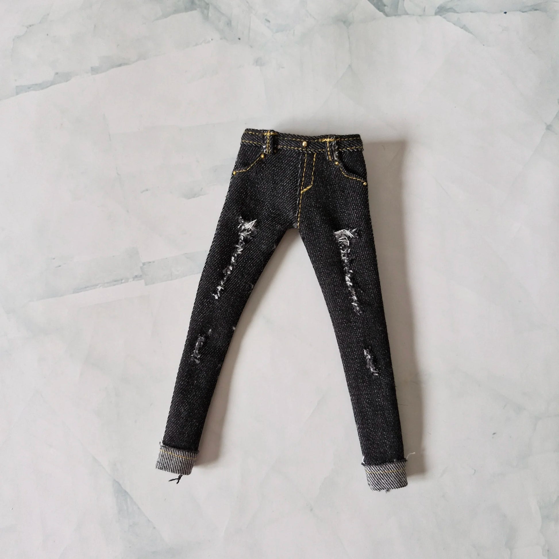 Flat lay view of black distressed skinny jeans with yellow stitching for Barbie dolls