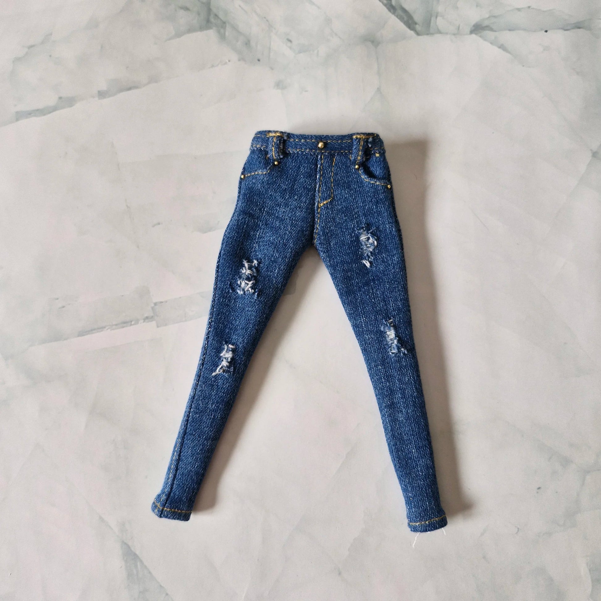 Flat lay view of medium blue distressed skinny jeans with gold stitching for Barbie dolls
