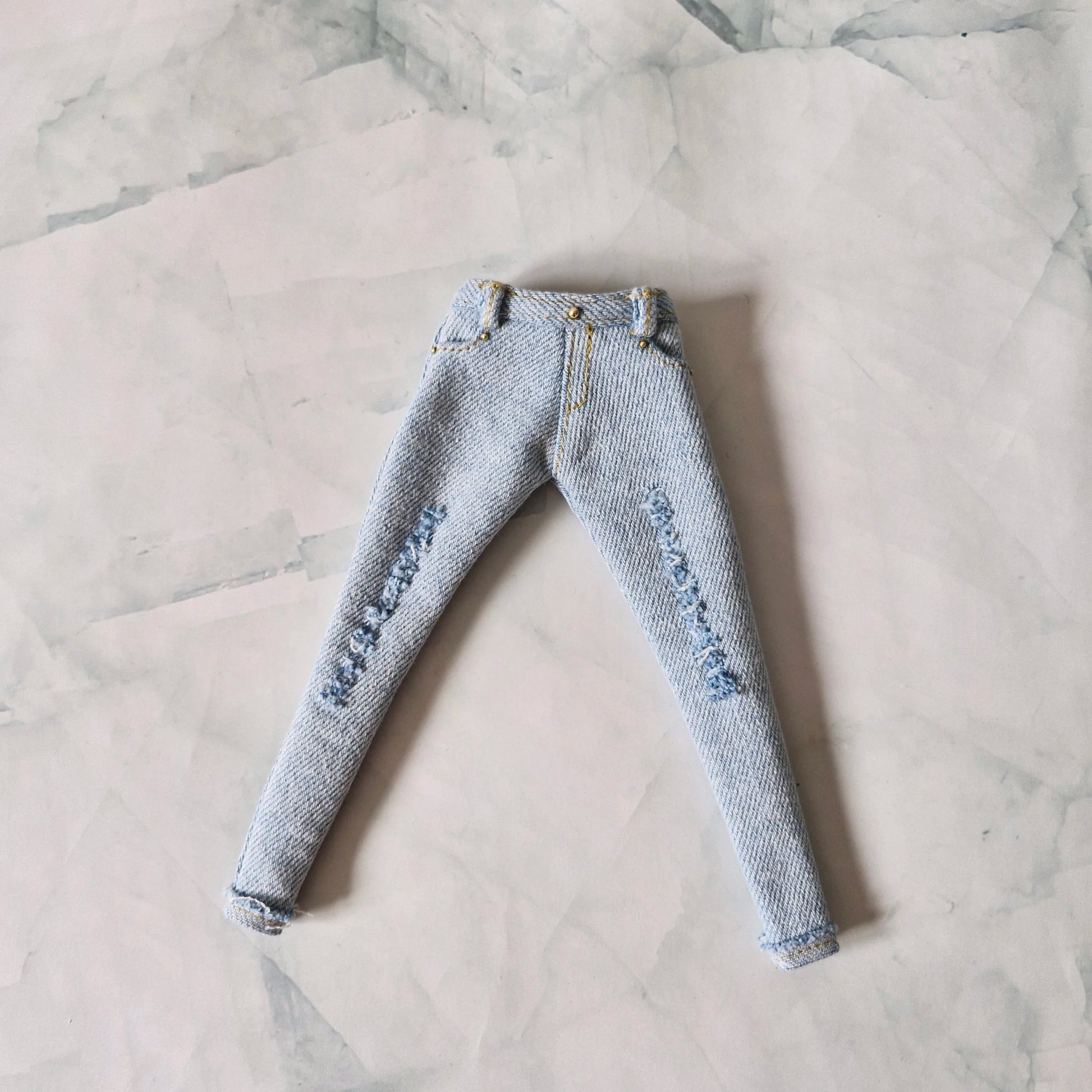 Flat lay view of light blue distressed skinny jeans with gold stitching for Barbie dolls