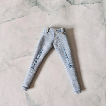 Flat lay view of light blue distressed skinny jeans with gold stitching for Barbie dolls