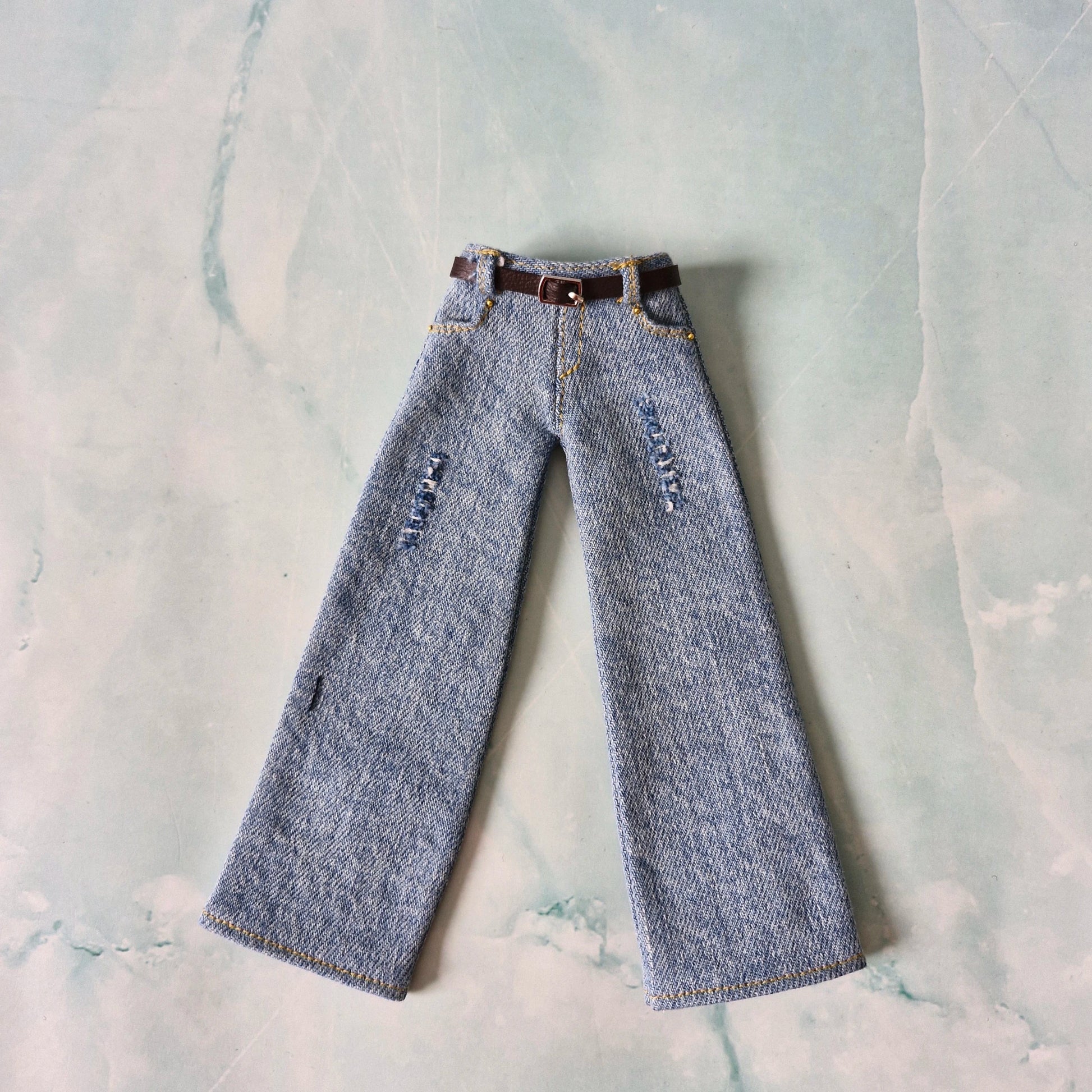 Pair of blue jeans with a belt on a textured light gray background