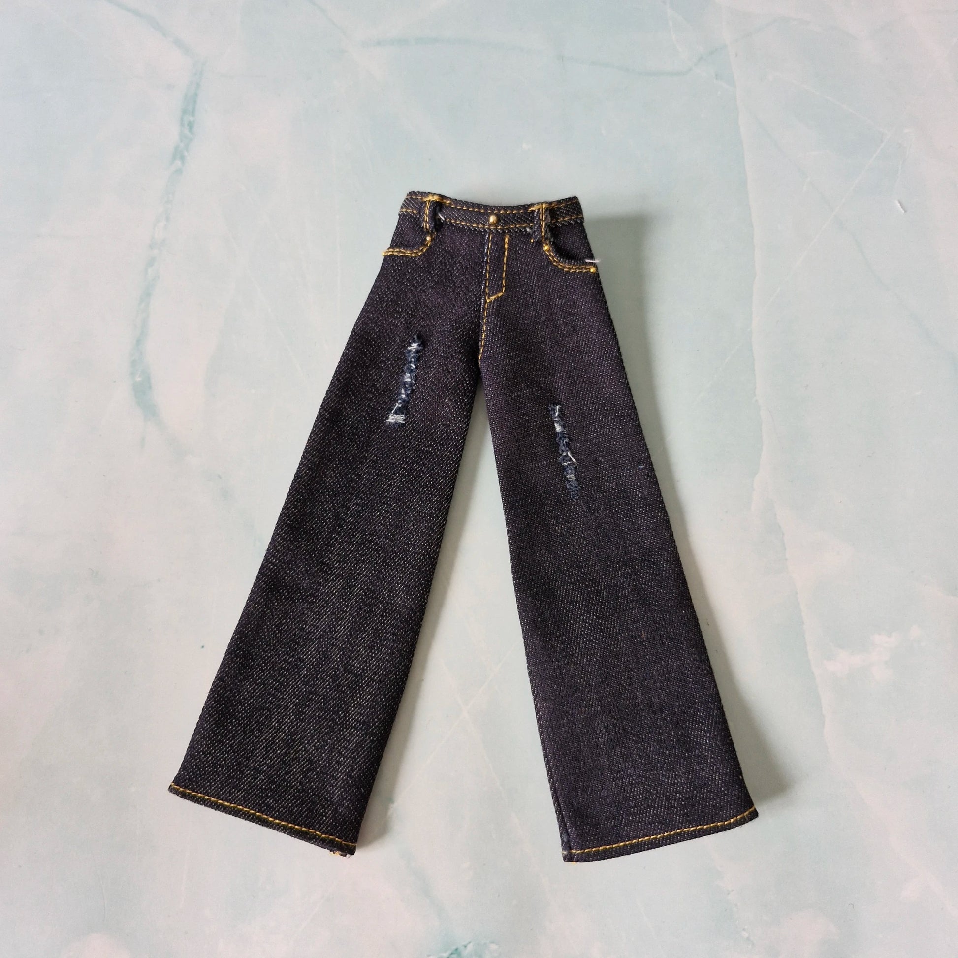 Pair of dark blue jeans with slight distressing on a light gray background